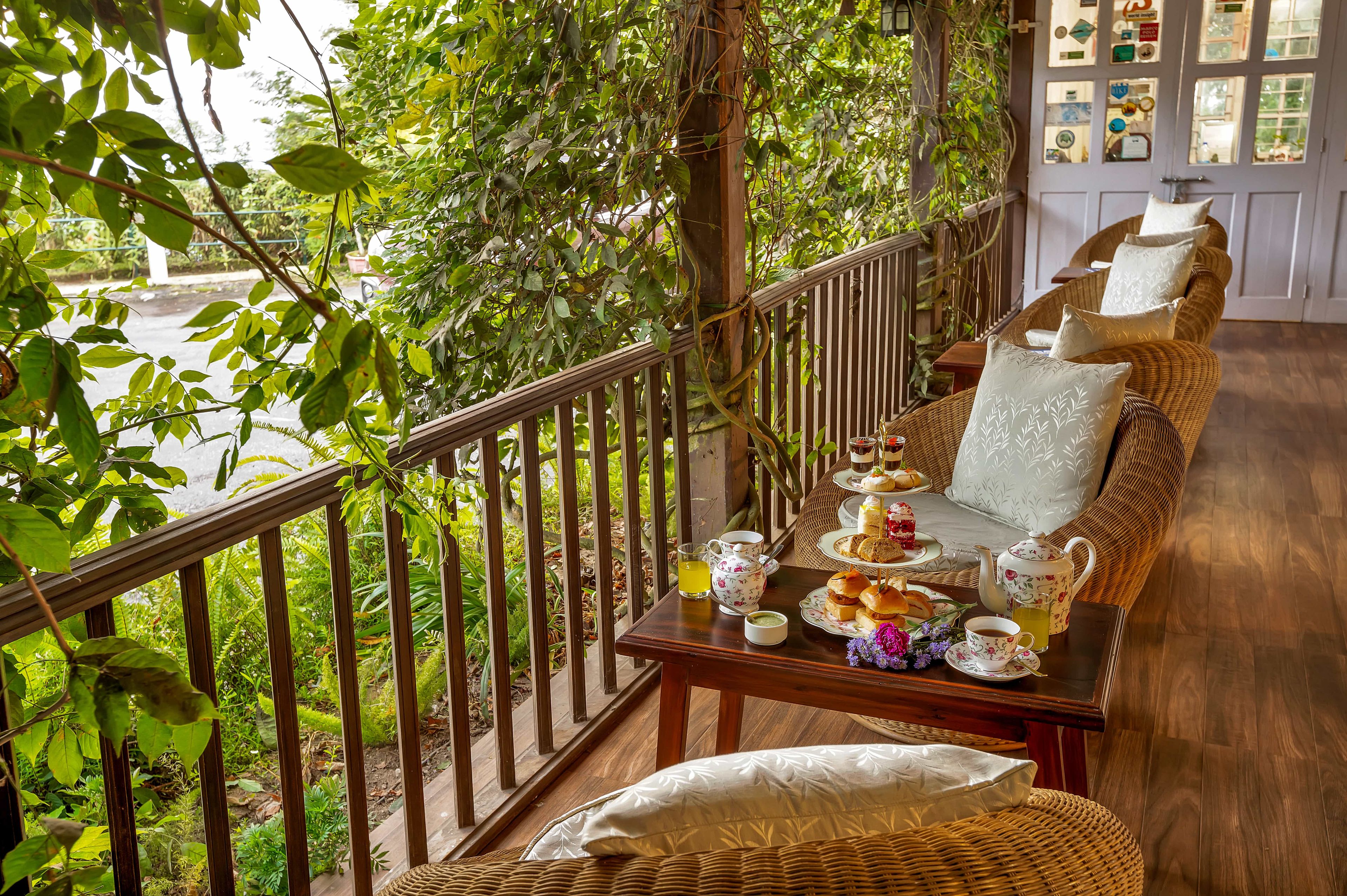 A balcony with a wicker sofa, a table with tea set, and a view of greenery.
