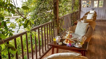 A balcony with a wicker sofa, a table with tea set, and a view of greenery.