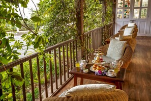 Un balcón con sofá de mimbre, una mesa con juego de té y vista a zonas verdes.