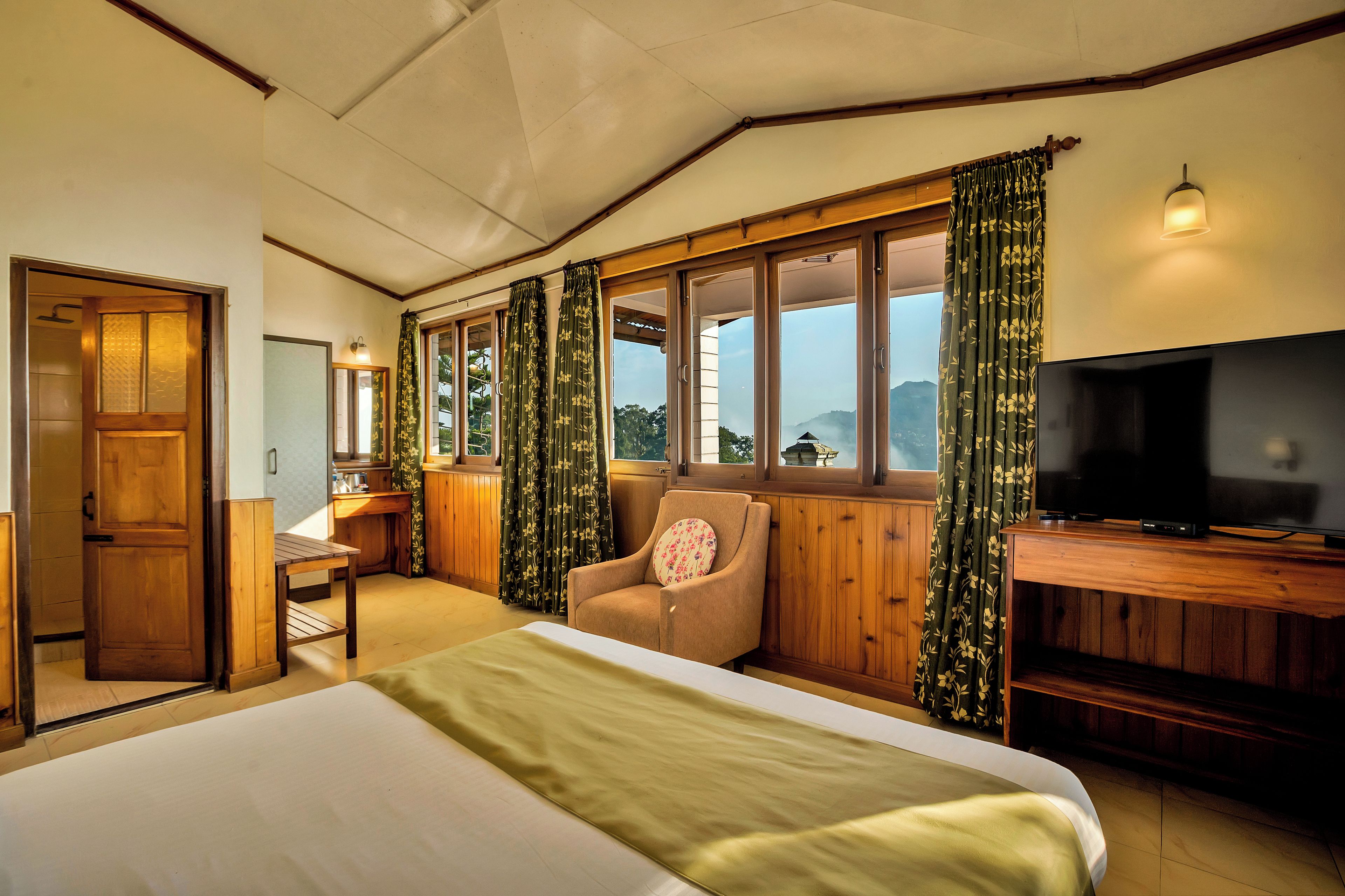 A bedroom with a bed, a television, a chair, and a window with curtains.