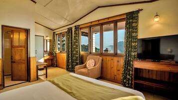 A bedroom with a bed, a television, a chair, and a window with curtains.