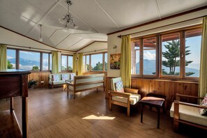A spacious room with wooden floors, large windows with curtains, and a view of mountains. - Sterling Park Kalimpong (Kalimpong)