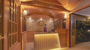 A wooden reception desk with a stone wall backdrop and a framed picture above it. - Sterling Park Kalimpong (Kalimpong)