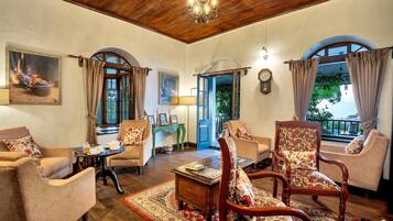A cozy living room with wooden flooring, a chandelier, and a view of the outdoors through arched windows.