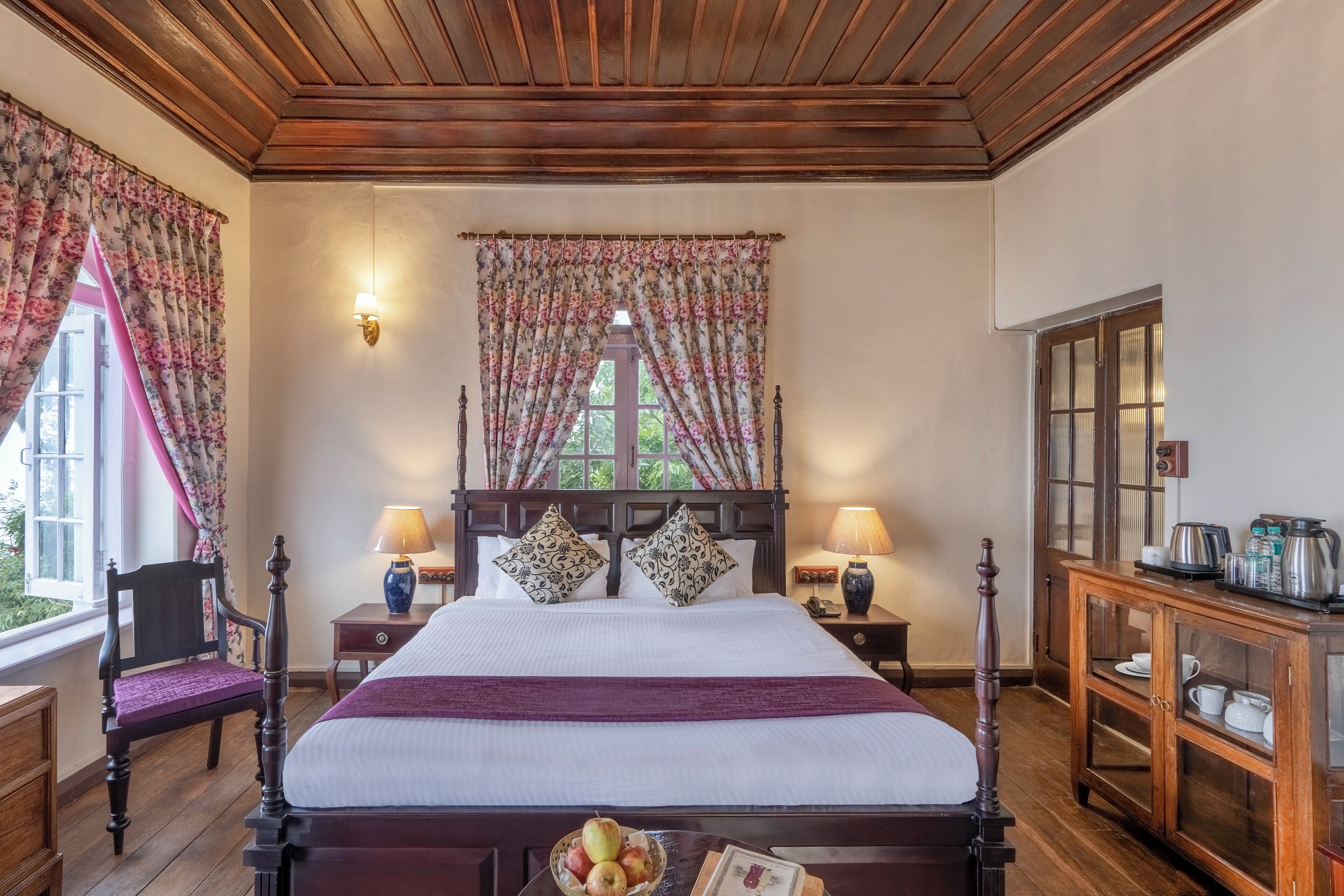 Un dormitorio tradicional con cama con dosel, cortinas florales, un aparador de madera y una ventana con vistas.