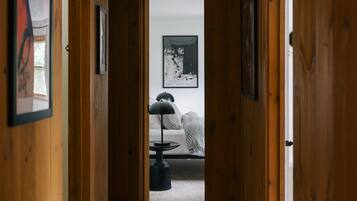 A wooden hallway leading to a bedroom with a bed, a ceiling fan, and framed pictures on the walls.