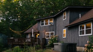 Une maison à deux étages avec une terrasse, entourée d’arbres et d’une pelouse.