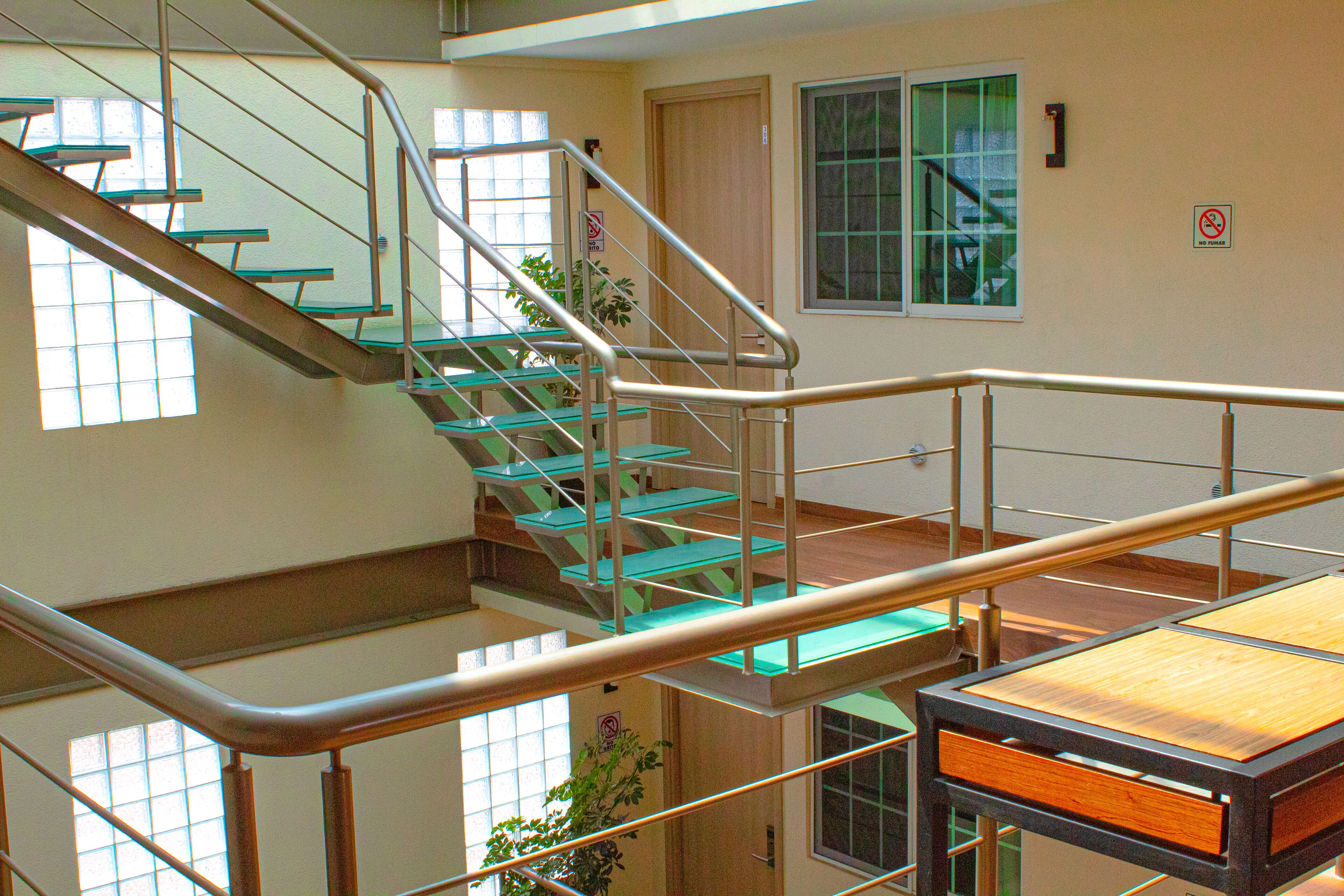 Un interior con varios niveles, una escalera, barandillas metálicas y una mesa de madera.