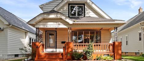 A two-story house with a porch, a front door, and a large window.