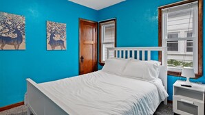 Un dormitorio con cama, mesita de noche, ventana y dos obras de arte en la pared.
