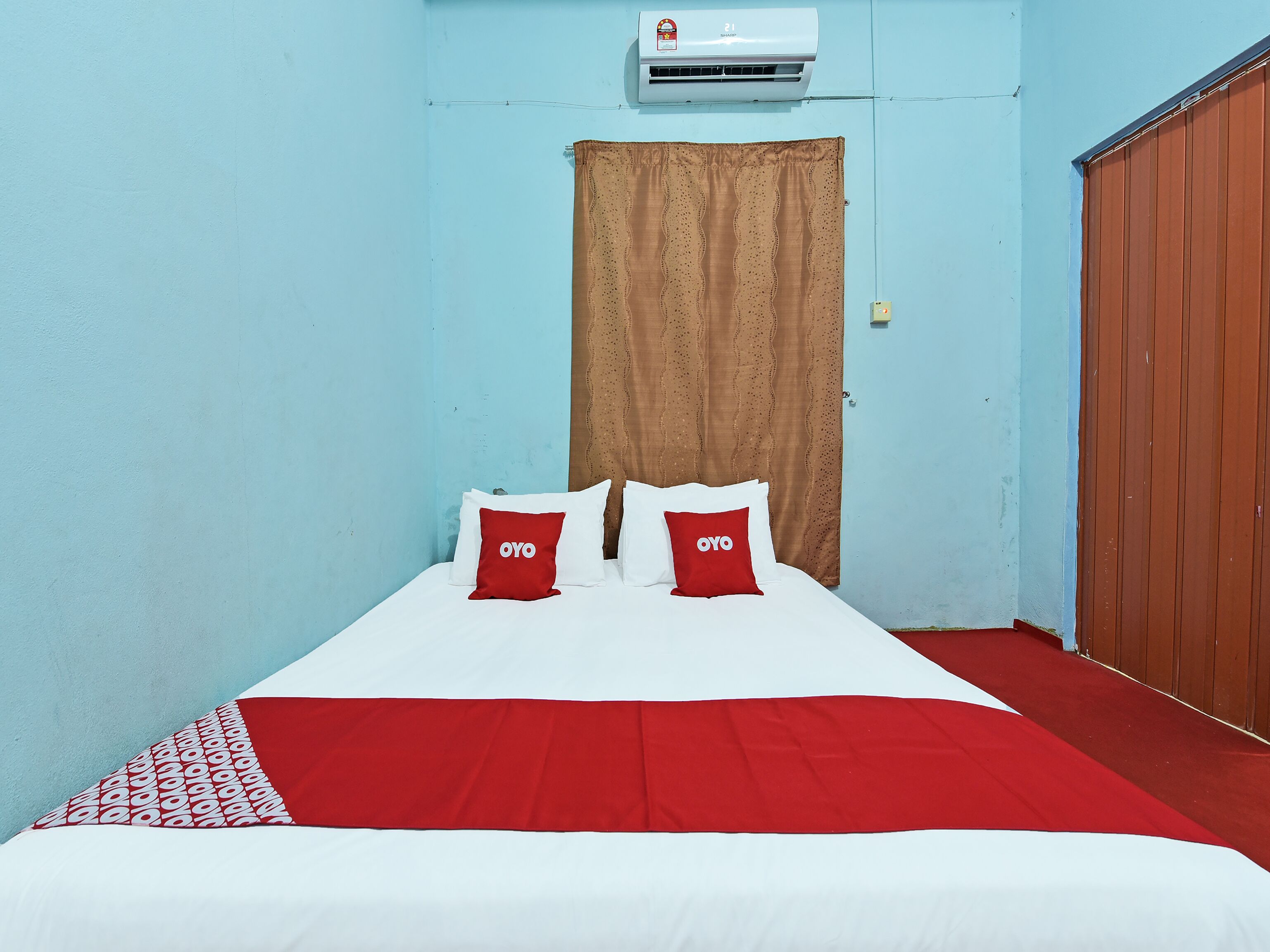 Una cama individual con ropa de cama blanca y roja, dos almohadas rojas con el logotipo 