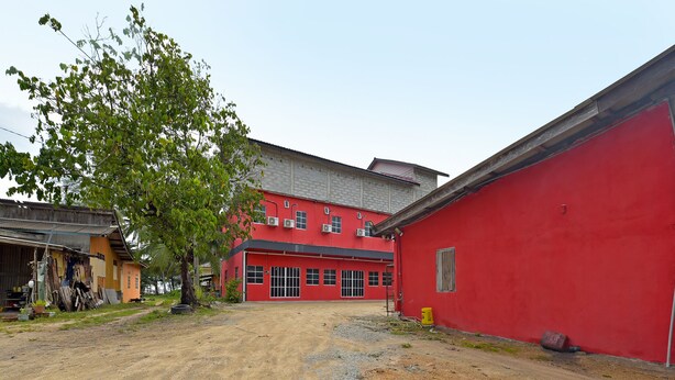 A red building with a dirt driveway and a tree in front. - OYO 90664 Rabi Hotel (Bachok)