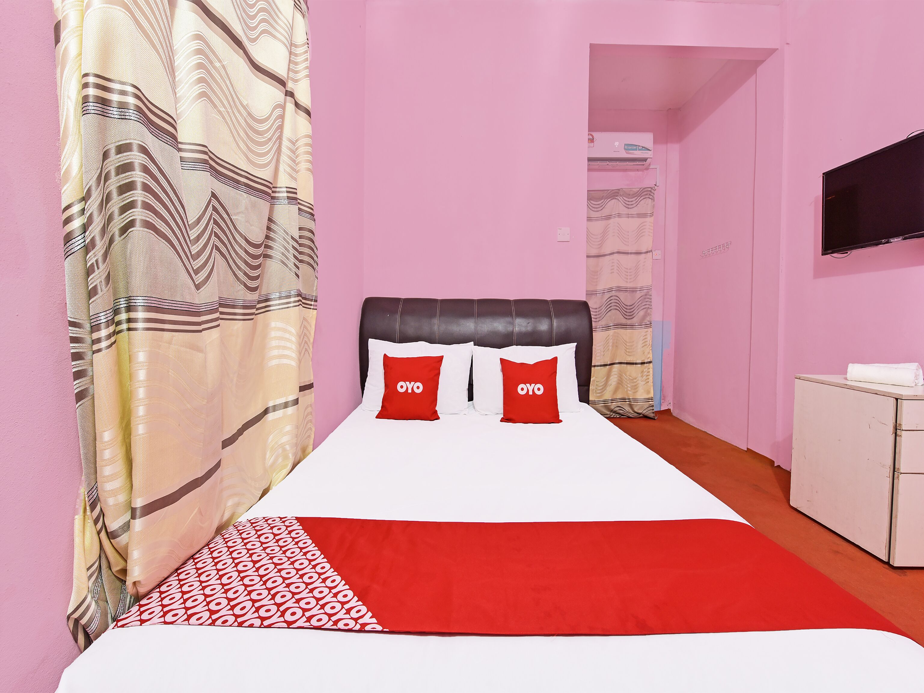 A hotel room with a bed, a TV mounted on the wall, and a white wardrobe.