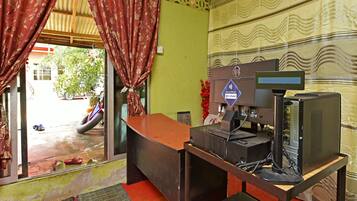 A room with a wooden desk, a computer, and a television. There is a window with curtains, a door, and a green wall with a patterned design.