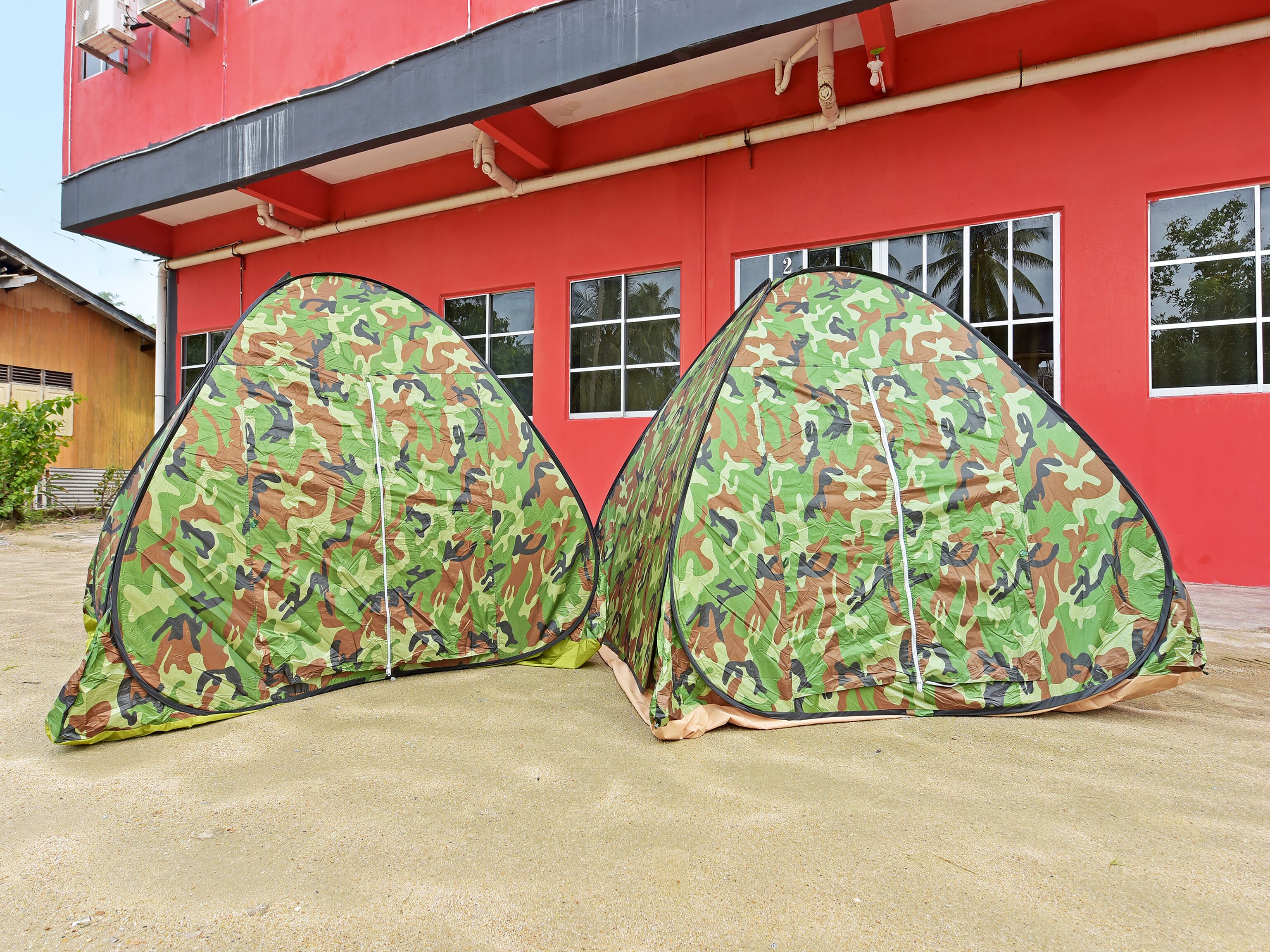 Two camouflage tents set up in front of a red building with multiple windows.