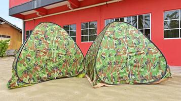 Two camouflage tents set up in front of a red building with multiple windows.
