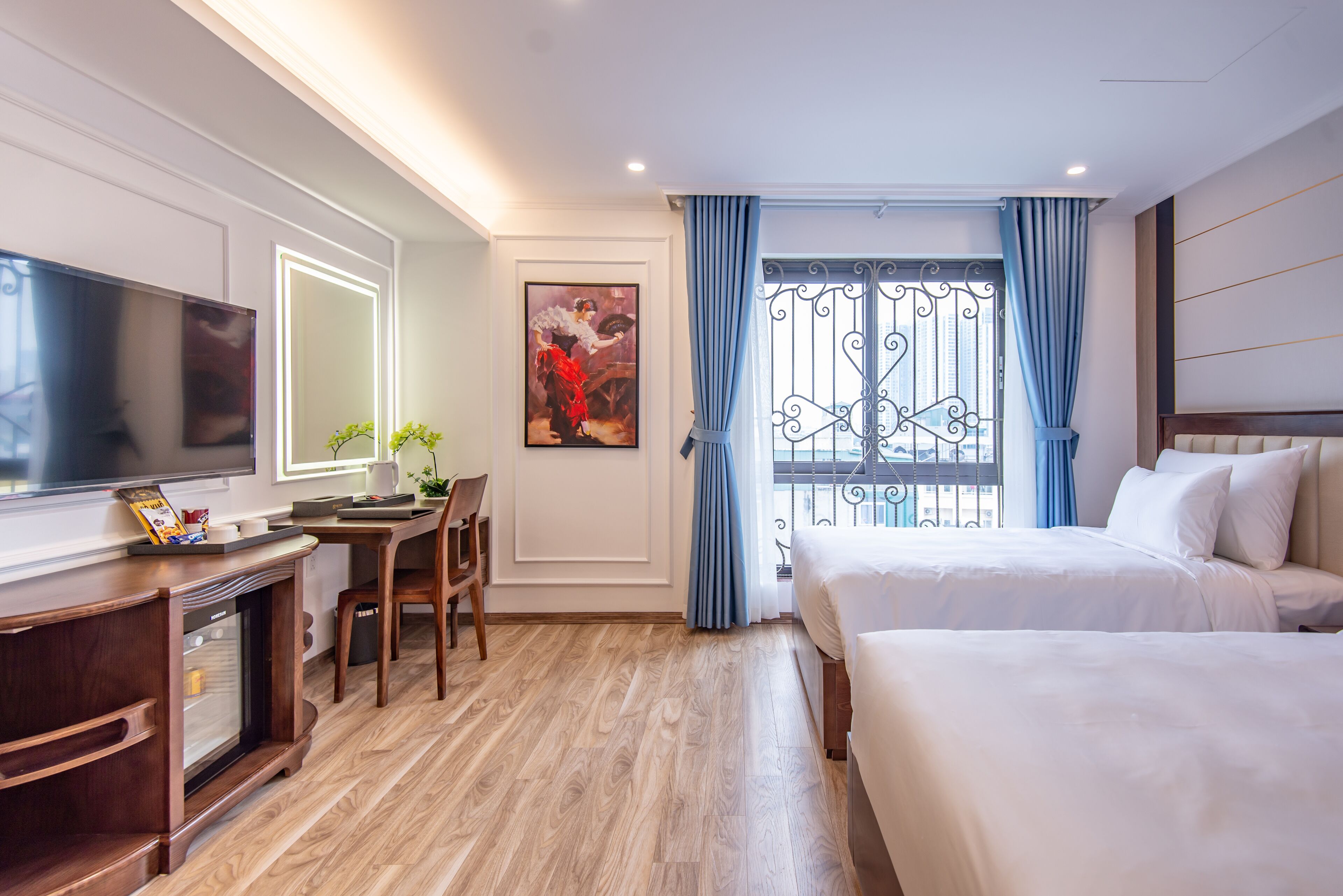 Habitación de hotel con televisión, escritorio, silla, dos camas y ventana con cortinas.
