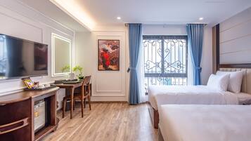 Habitación de hotel con televisión, escritorio, silla, dos camas y ventana con cortinas.