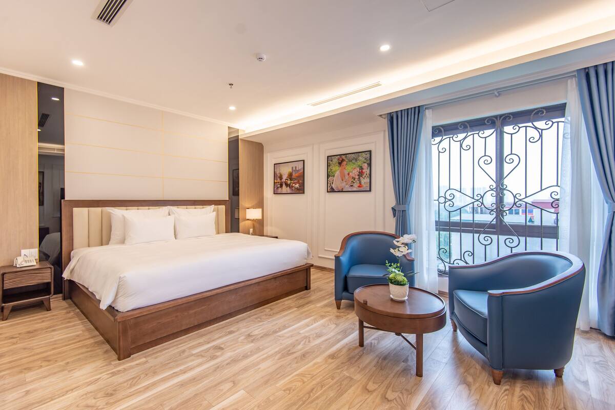 A hotel room with a large bed, a desk, two chairs, and a window with curtains.