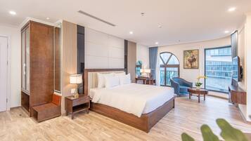 Une chambre d’hôtel moderne dotée d’un grand lit, d’un coin salon avec un fauteuil et une petite table, d’une télévision et d’un balcon offrant une vue agréable.