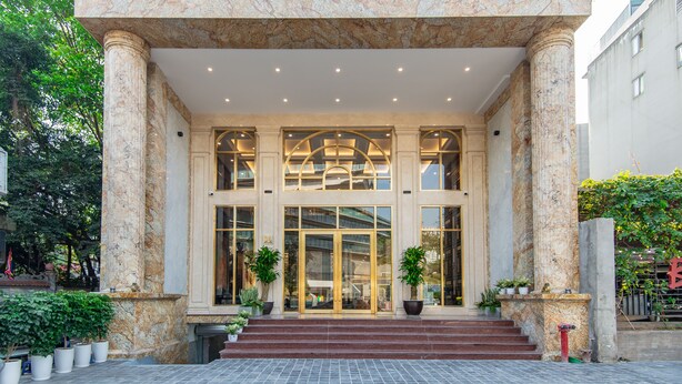 Exterior do Hotel Reynaluxury com colunas de mármore, grandes portas de vidro e plantas em vasos.