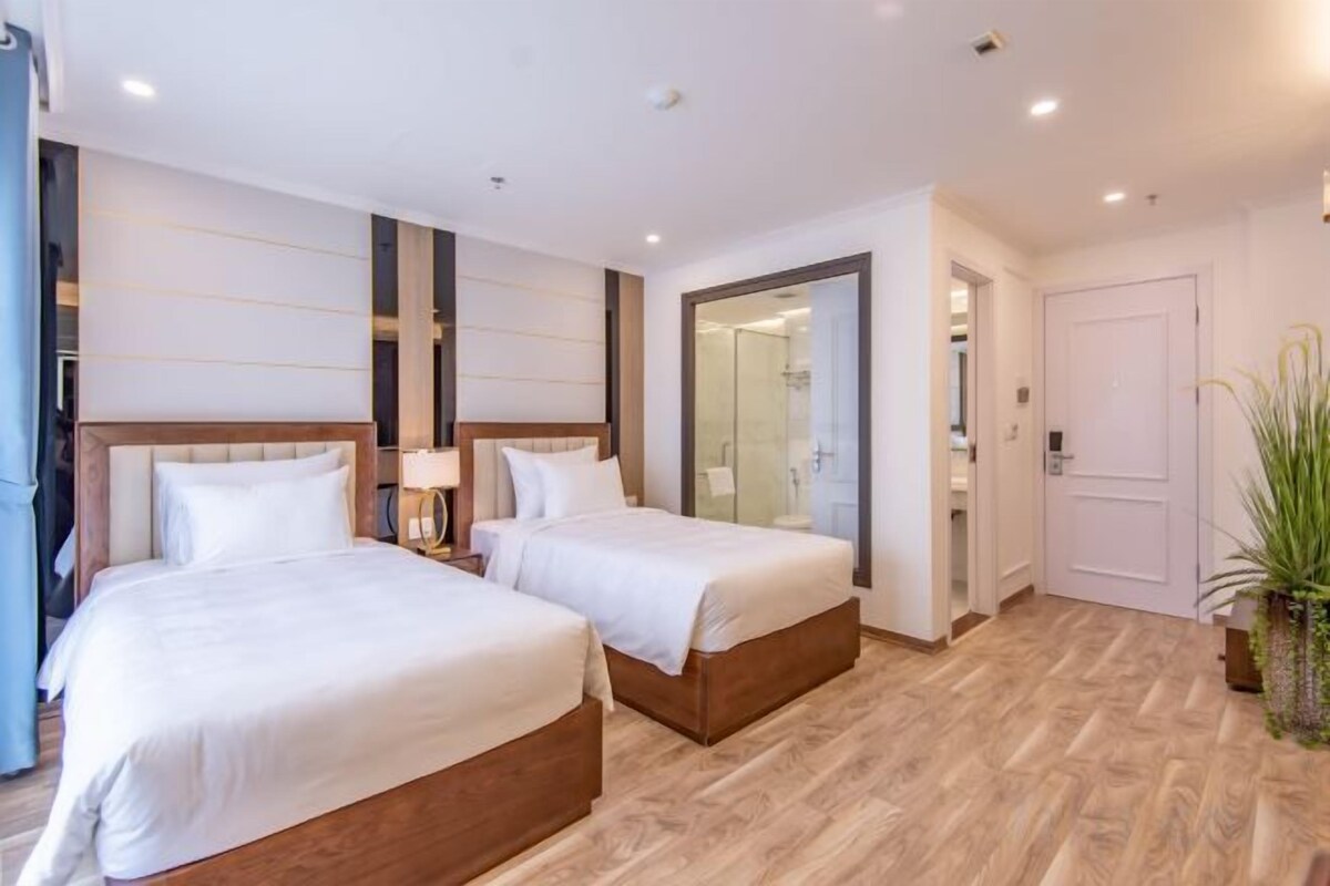 A hotel room with two beds, a wooden floor, a mirror, and a potted plant.
