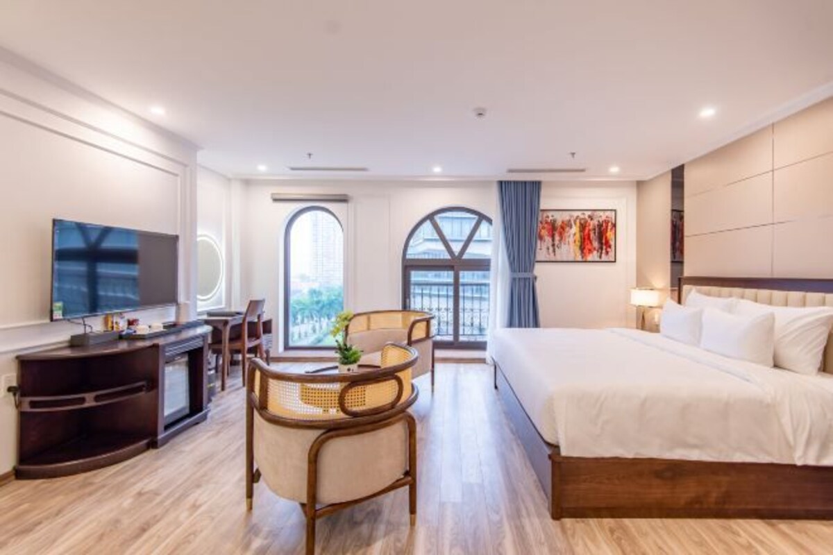A hotel room with a bed, a desk with a chair, a television, and a large window.