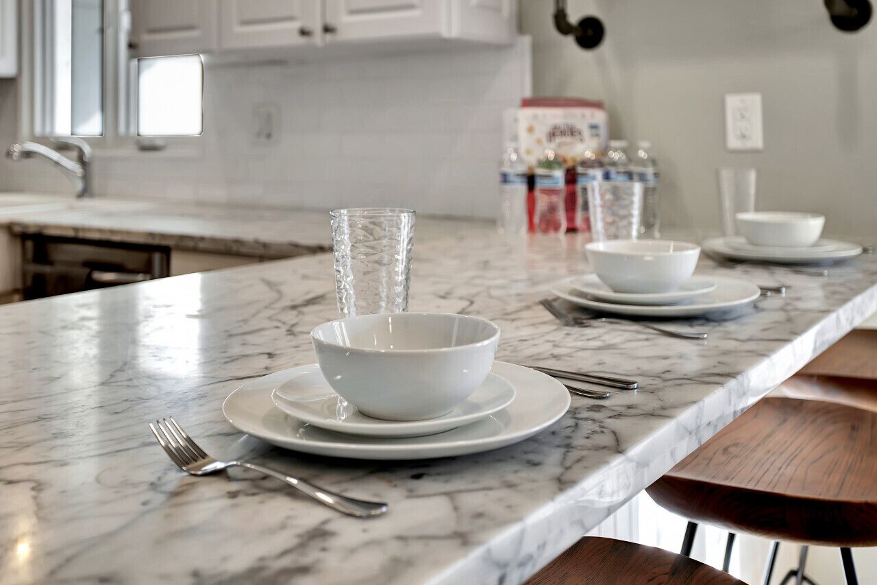 A kitchen with white cabinets, a marble countertop, and a dining area with a wooden bench.