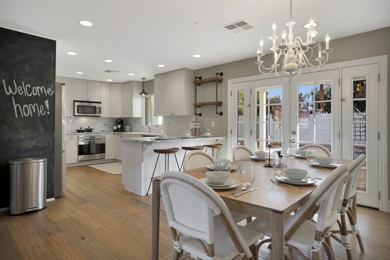 A modern kitchen with white cabinets, a central island, and a dining area with white wicker chairs.