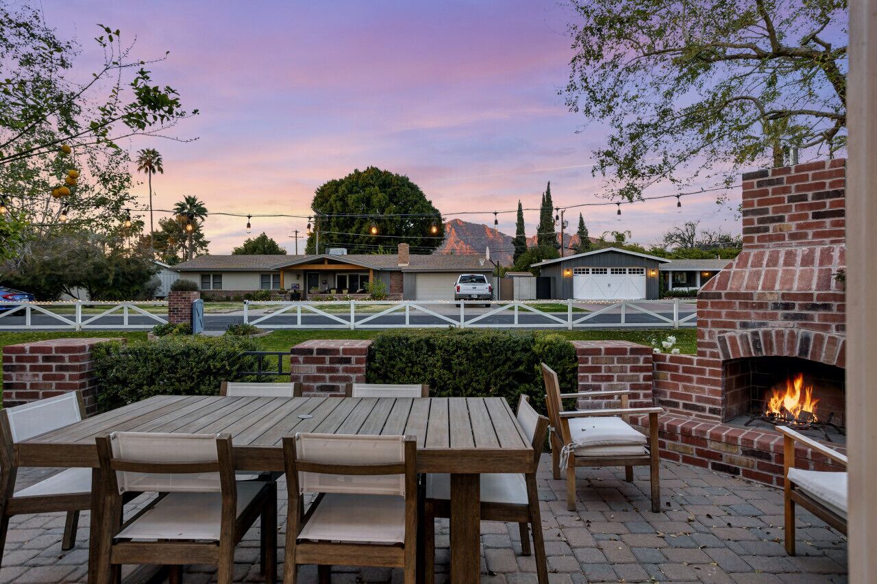 An outdoor patio with a brick fire pit, wooden tables and chairs, and a view of a mountain in the background.