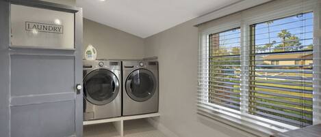 A laundry room with two front-loading washing machines, a built-in cabinet labeled 'laundry', and a window with blinds overlooking a residential area.