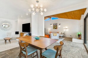 Een ruime eetruimte met een houten tafel en stoelen, een kroonluchter en een grote spiegel aan de muur.