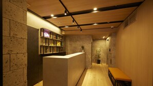 A reception area with a wooden reception desk, a bench, and a wall-mounted shelf with items. - Section L Hatchobori (Tokyo)