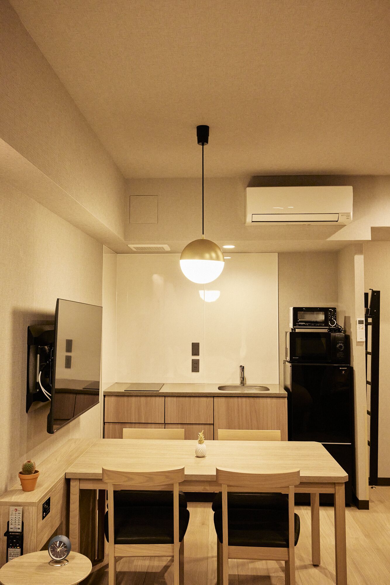 A compact kitchen with a dining table, chairs, a hanging light fixture, a built-in oven, a microwave, and a refrigerator.