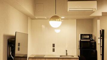 A compact kitchen with a dining table, chairs, a hanging light fixture, a built-in oven, a microwave, and a refrigerator.
