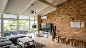 Een ruime woonkamer met een bakstenen muur, een grote televisie, een bank, een bijzettafeltje en een gitaar.