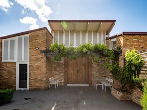 A brick building with a wooden door, white shutters, and a pergola with vines. There are two white chairs outside. - Mars: The Menangle Hideaway: Relax and Unwin (Menangle)