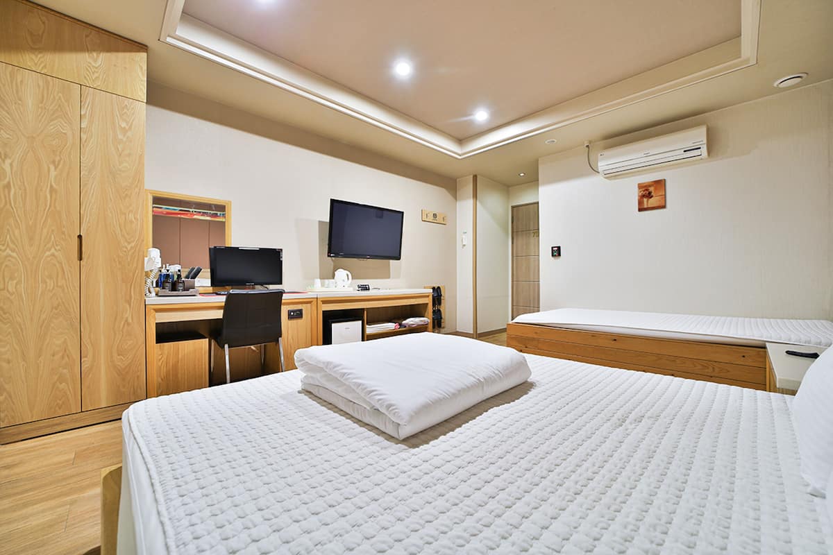 A hotel room with a bed, a desk, a chair, a television, and an air conditioning unit.