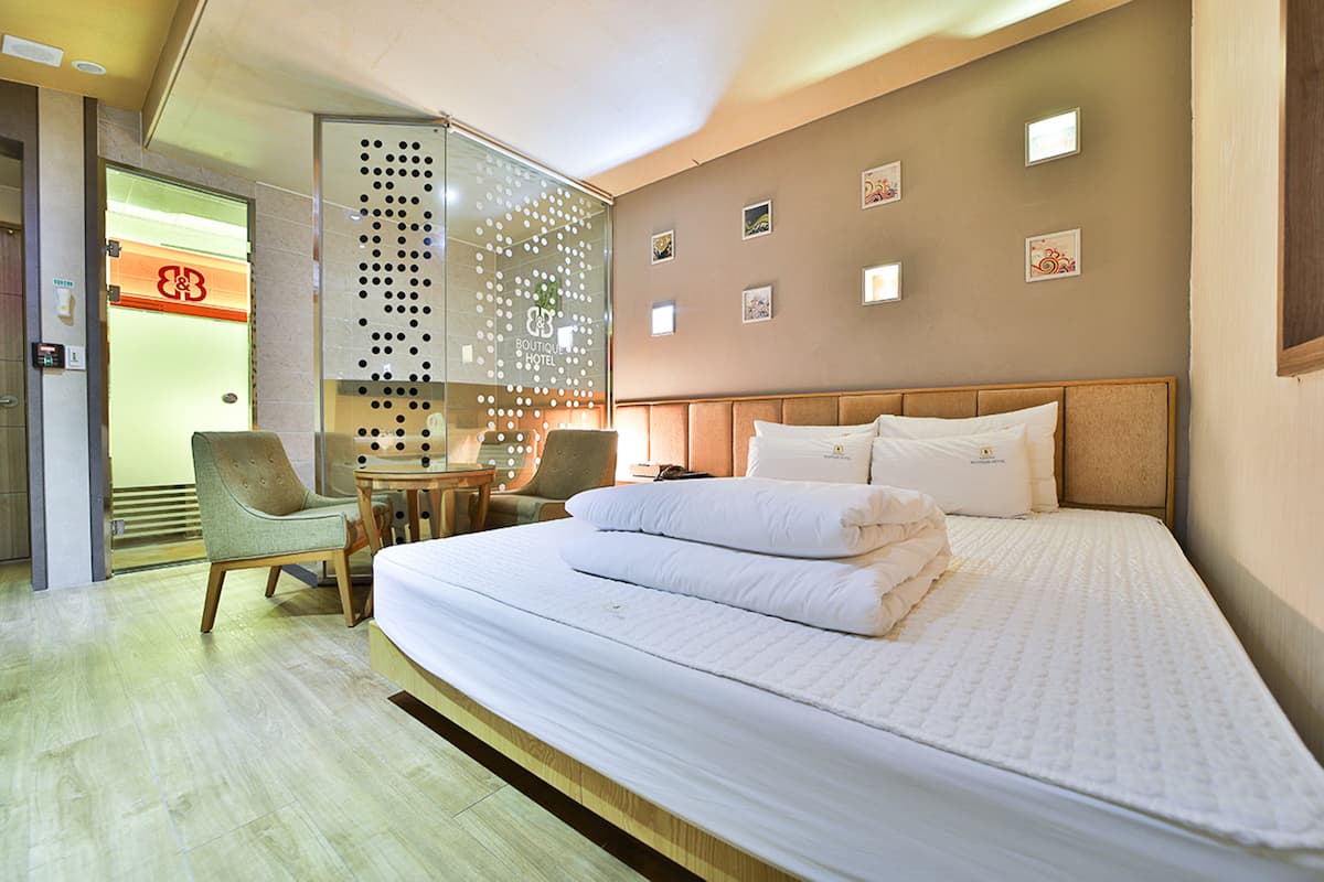 A hotel room with a large bed, a desk, and a chair. There are pictures on the wall and a glass partition with a pattern.