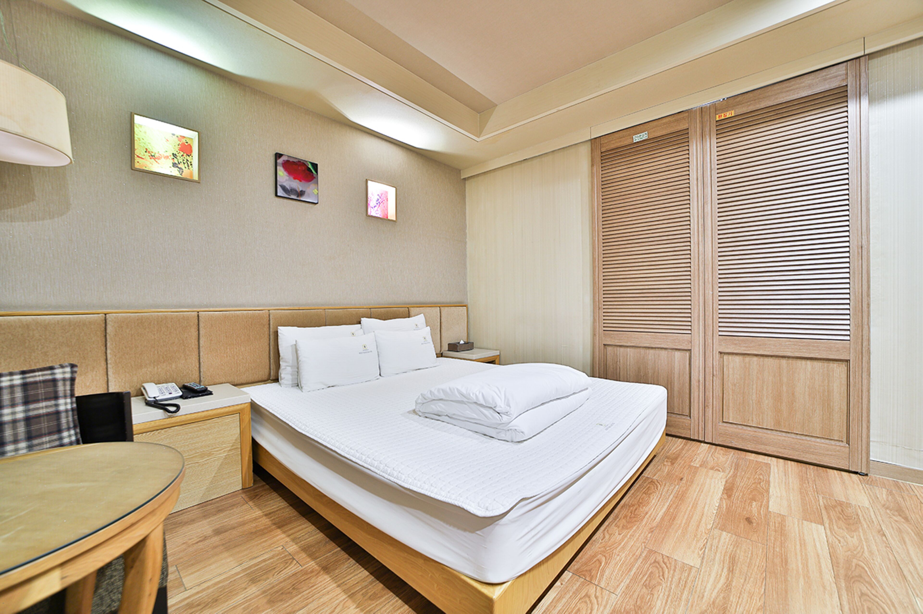 A hotel room with a bed, bedside table, lamp, and artwork on the wall.