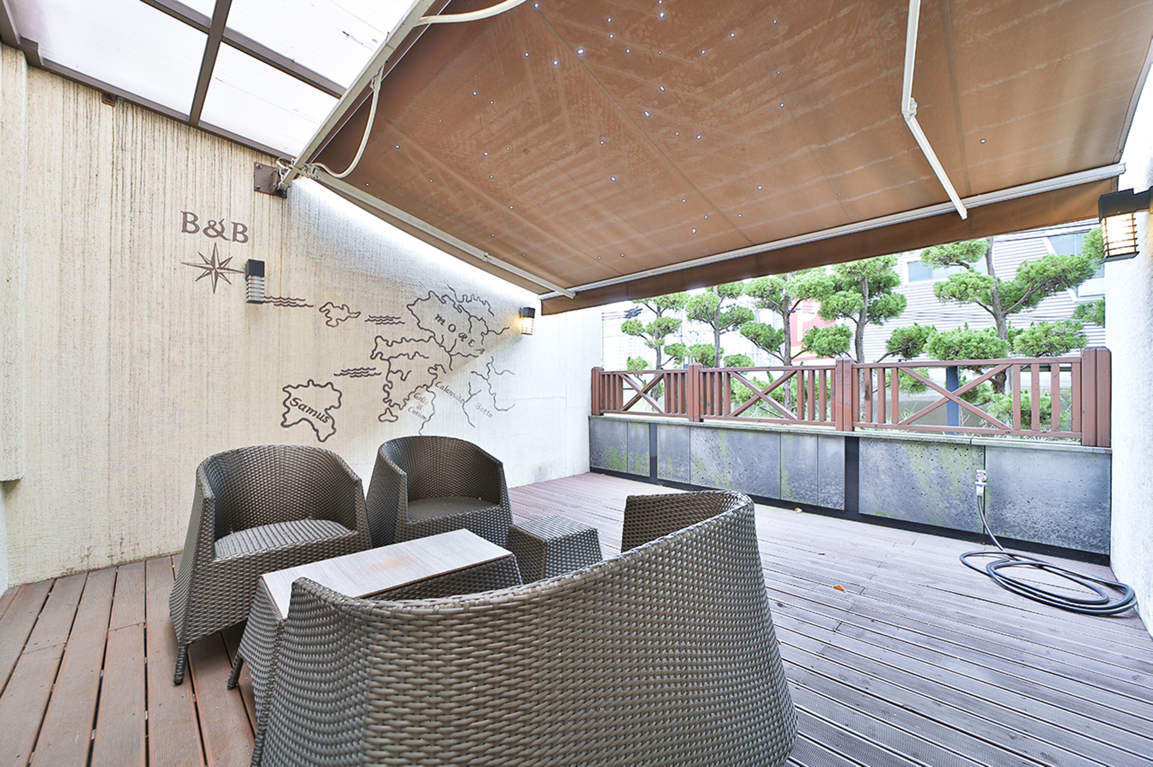 Un espacio al aire libre con mobiliario de mimbre, una terraza de madera y una pared con un mapa y el logotipo de B&B.