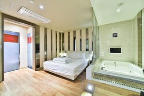 Quarto de hotel moderno com uma cama grande, banheiro separado com hidromassagem e divisória de vidro.