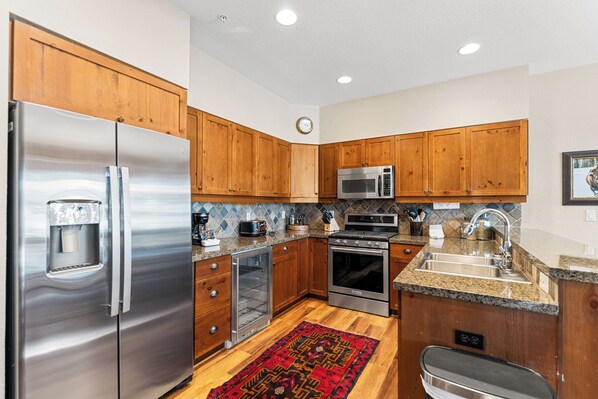 A modern kitchen with wooden cabinets, stainless steel appliances, and a red patterned rug.