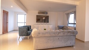 A modern living room with a large grey sofa, a smaller armchair, and a cabinet with decorative items.