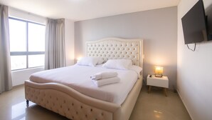 A neatly arranged bedroom with a large bed, a bedside table with a lamp, and a TV mounted on the wall.