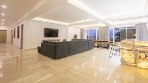 A spacious living area with a large dark-colored sofa, a flat-screen TV mounted on the wall, and a marble accent wall. - 7 Bedroom in Clock Tower Plaza with Private Pool (Cartagena)