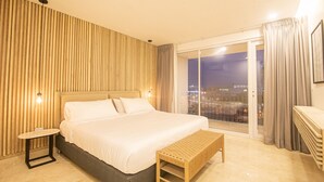 A modern hotel room with a large bed, a small table, and a bench. The room has a city view through a large window. - 7 Bedroom in Clock Tower Plaza with Private Pool (Cartagena)