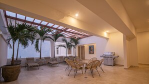 A spacious indoor area with a high ceiling, large potted plants, wicker furniture, and a grill station. - 7 Bedroom in Clock Tower Plaza with Private Pool (Cartagena)