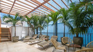 A covered outdoor seating area with wicker chairs and a wooden table, surrounded by potted plants and a blue wall. - 16 Bedroom in Clock Tower Plaza with Private Pool (Cartagena)