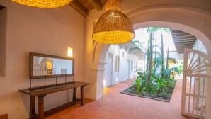 Un pasillo con un banco, una lámpara colgante y vistas a un patio con plantas y una puerta.